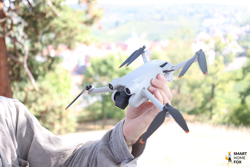 Die DJI Mini 3 Pro wird in der Hand gehalten und ist hellgrau und die Rotorblätter sind schwarz mit einem Orangestich.